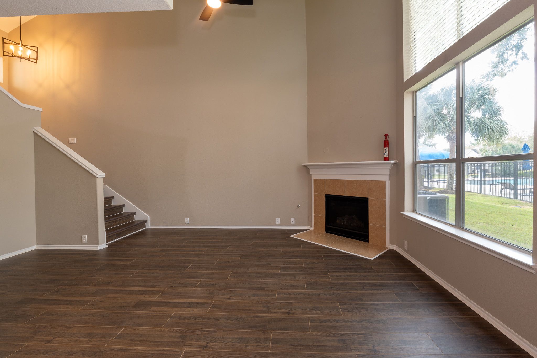 Two-story living room with dark wood-look floor, corner fireplace and tall windows