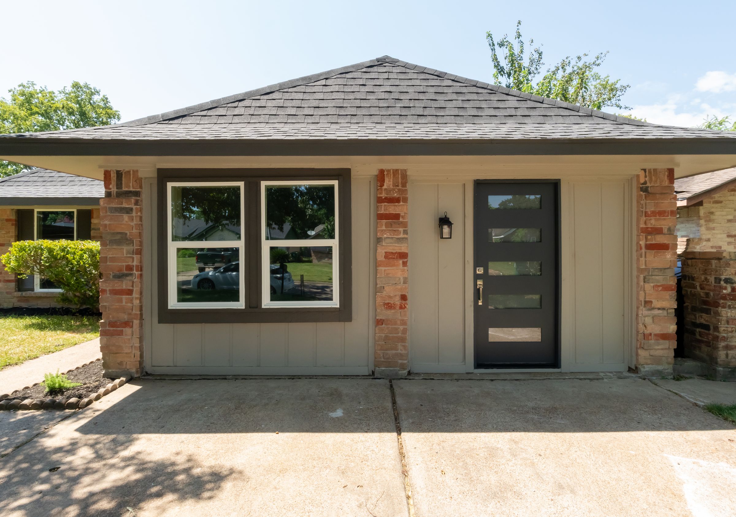 Front of the finished house: greige board-and-batten between original brick piers, white windows with bronze trim, modern black five-lite door