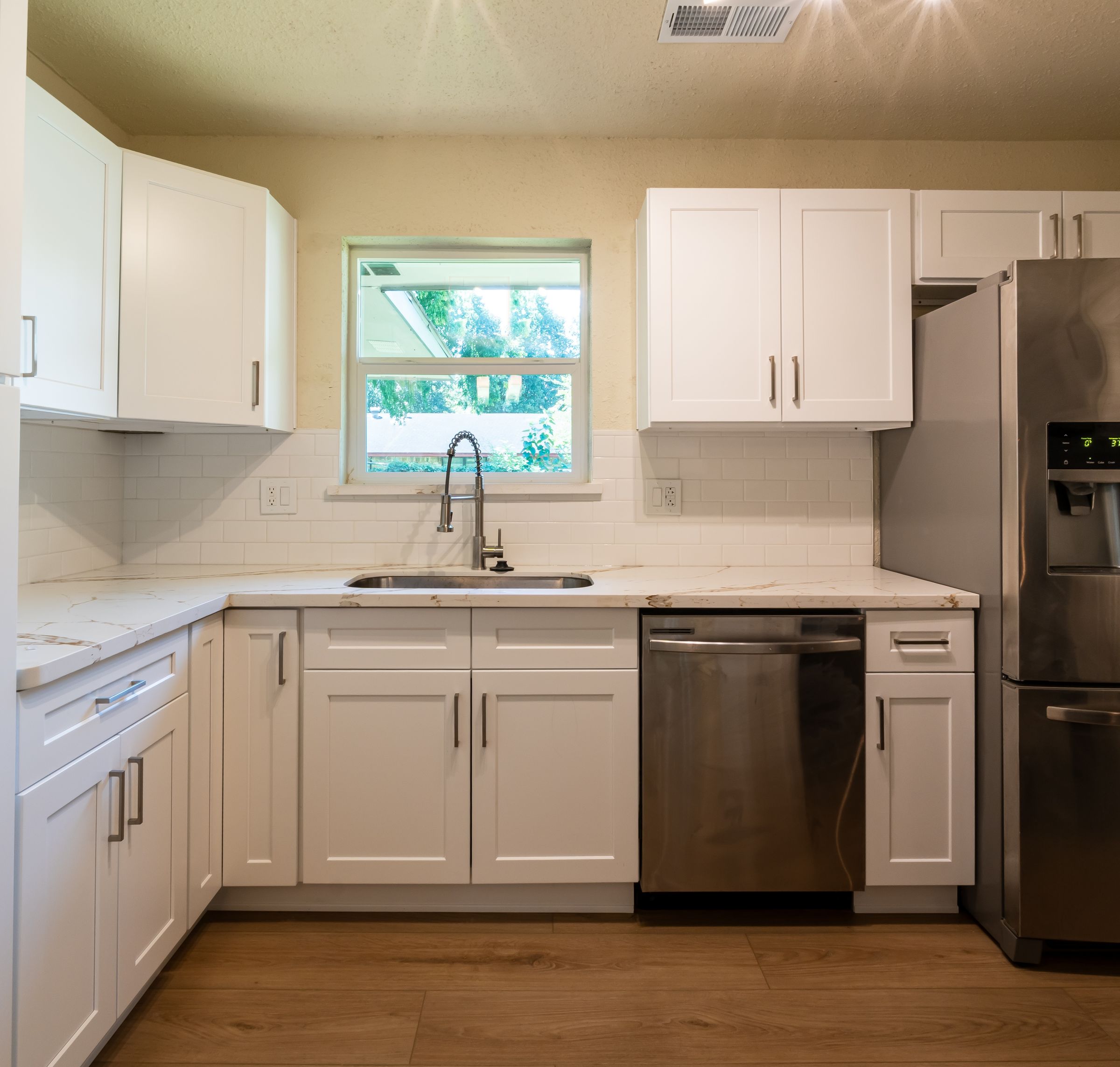 Finished kitchen with white shaker cabinets, white-veined counters, subway tile and warm wood-look floor