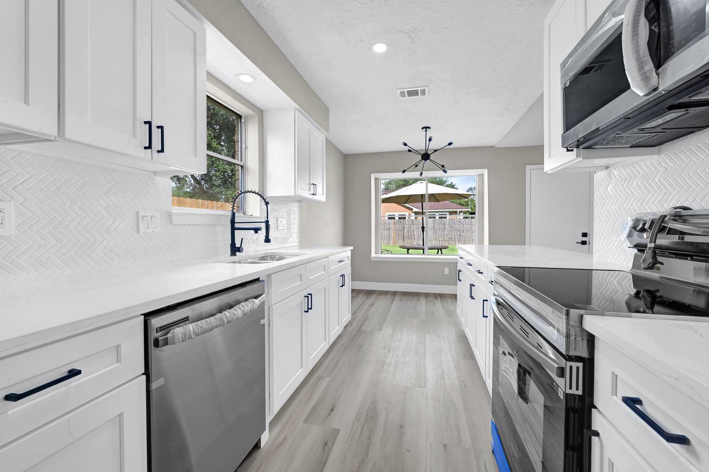 Galley kitchen with white shaker cabinets, matte-black pulls and faucet, white quartz and herringbone backsplash